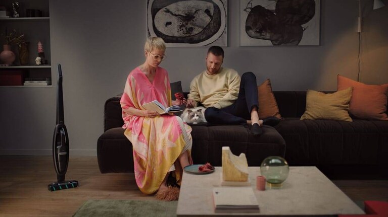 Un couple dans un salon avec un aspirateur sans fil en arrière-plan.