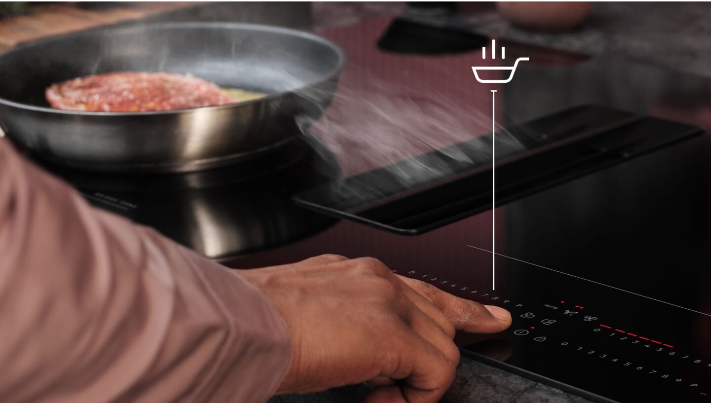 Un doigt touche le panneau de commande de la taque de cuisson.