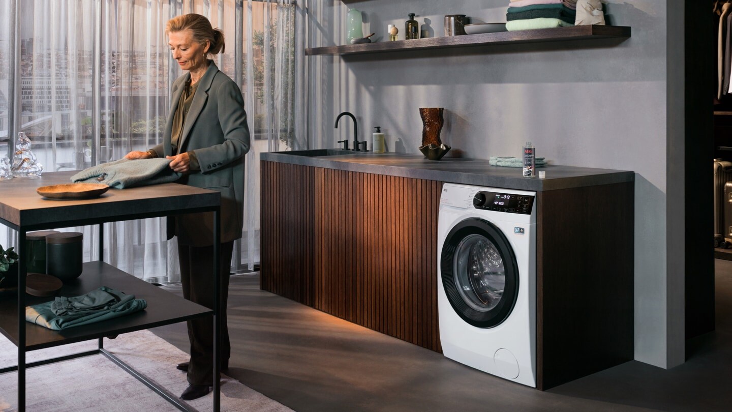 Femme pliant un sweat-shirt dans une buanderie devant un lave-linge séchant