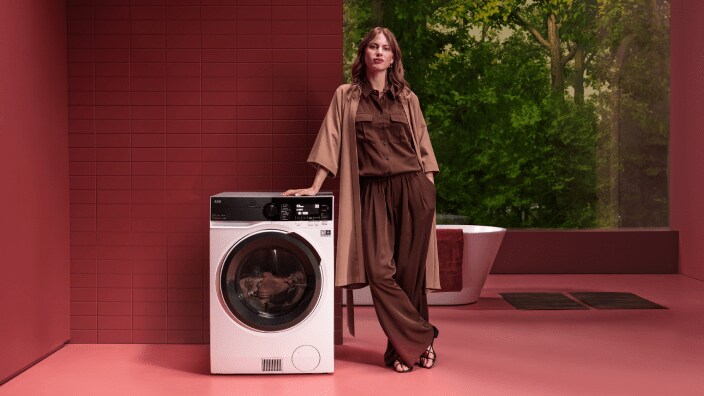 Femme debout à côté d'une machine à laver AEG.