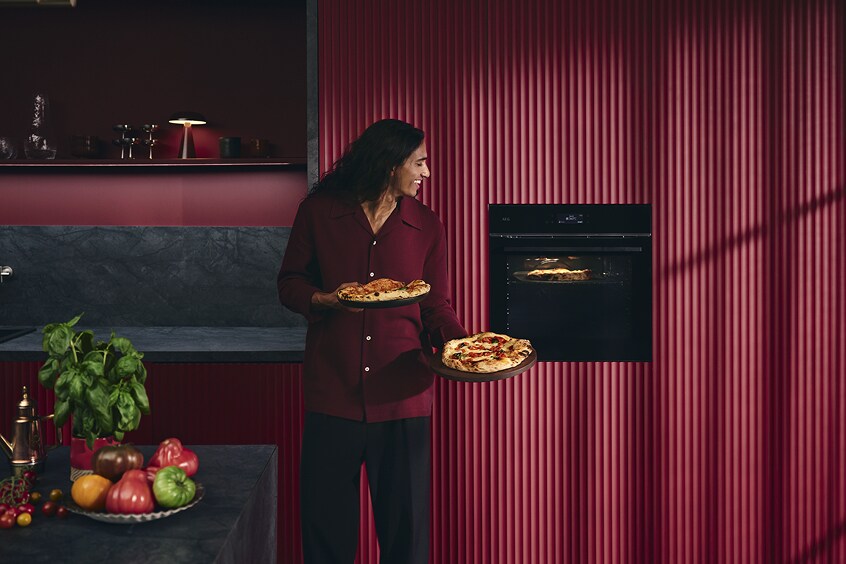 Femme tenant une pizza près du four