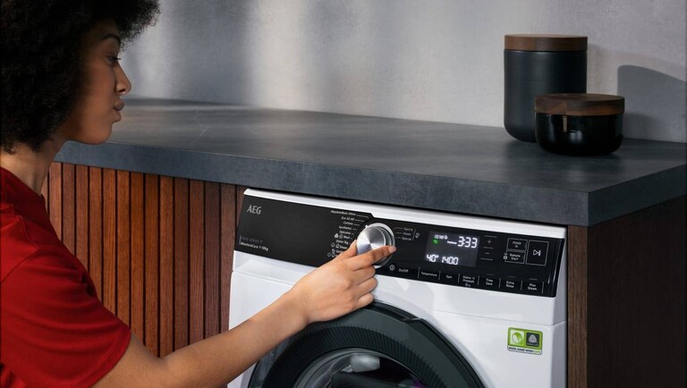 Femme réglant le cycle de lavage à 30 degrés sur un lave-linge AEG